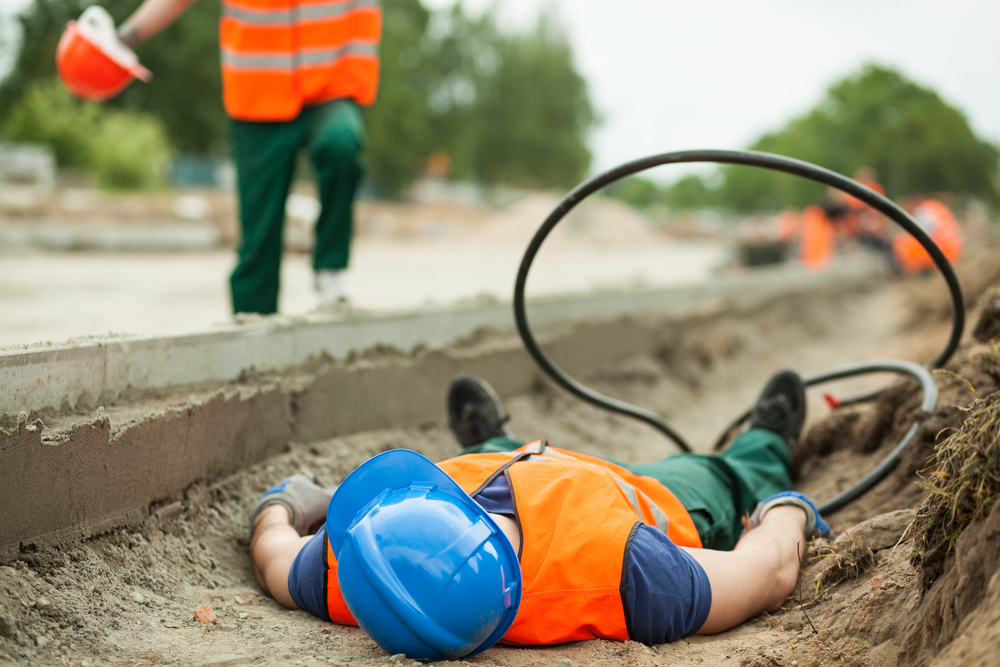 A man lies on the ground, holding a garden hose, surrounded by grass and plants.