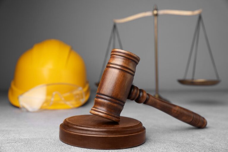 A hard hat, gloves, and a gavel arranged on a table, symbolizing safety and authority in a construction or legal context.