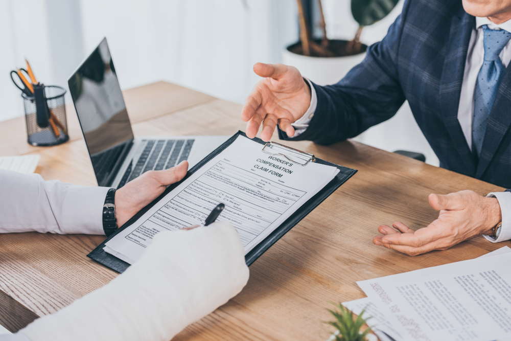 A man in a suit holds a document, while another man beside him holds a pen, indicating a discussion or agreement.